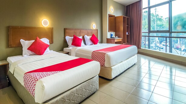 A hotel room with two beds, each with red and white bedding, a nightstand, a dresser, and a large window offering a view of the outside. - Super OYO 828 Comfort Hotel Shah Alam (Shah Alam)