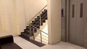 Un ascenseur moderne doté d’un écran numérique, un escalier avec des rampes en métal et un sol carrelé et impeccable.