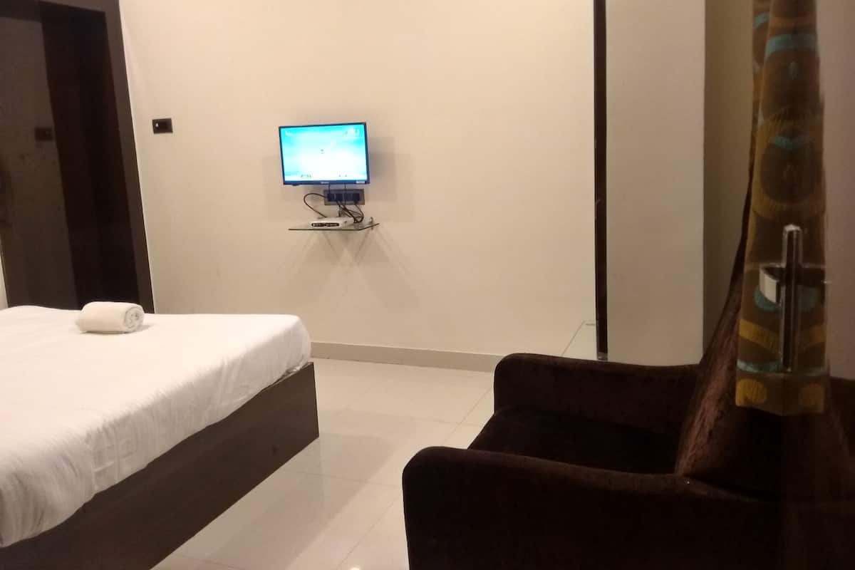 Une chambre d’hôtel avec un lit, un téléviseur fixé au mur et une chaise.