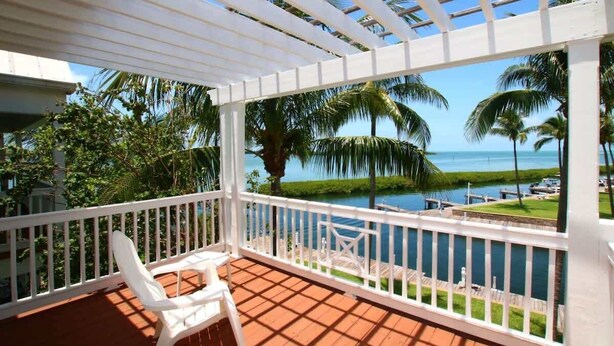 A covered outdoor area with a view of a body of water and palm trees. - Marathon Townhome | Boat Slip + Pool | Gulf Access (Marathon)