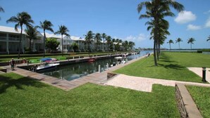 A marina with boats docked, a grassy area with palm trees, and a building with balconies. - Marathon Townhome | Boat Slip + Pool | Gulf Access (Marathon)