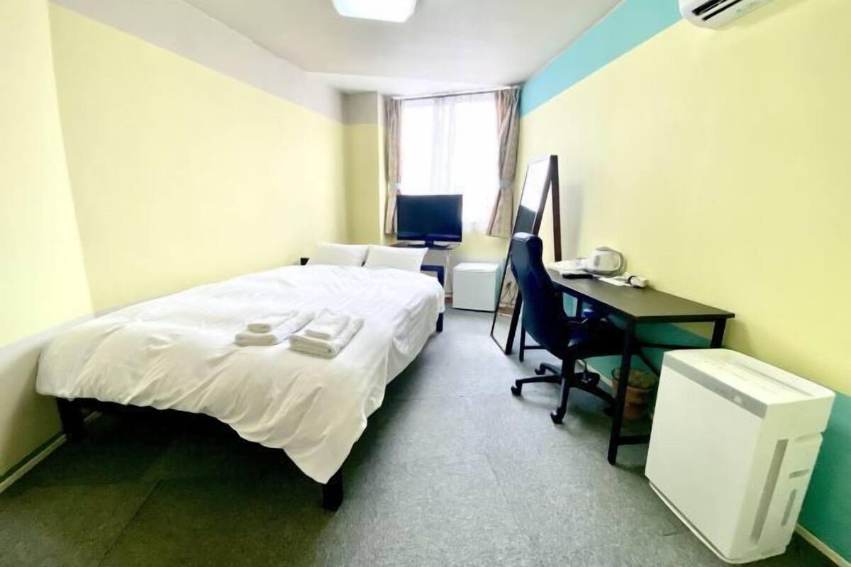 A hotel room with a bed, a desk, a chair, a television, and an air conditioning unit.