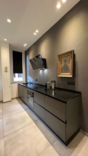 A modern kitchen with a built-in island, recessed ceiling lights, a window with a blind, and a framed picture on the wall. - Apartment via Ferrucci 22 (Milan)