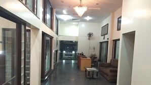 A spacious hallway with a polished floor, a reception desk, a seating area with a sofa and a small table, and a chandelier.