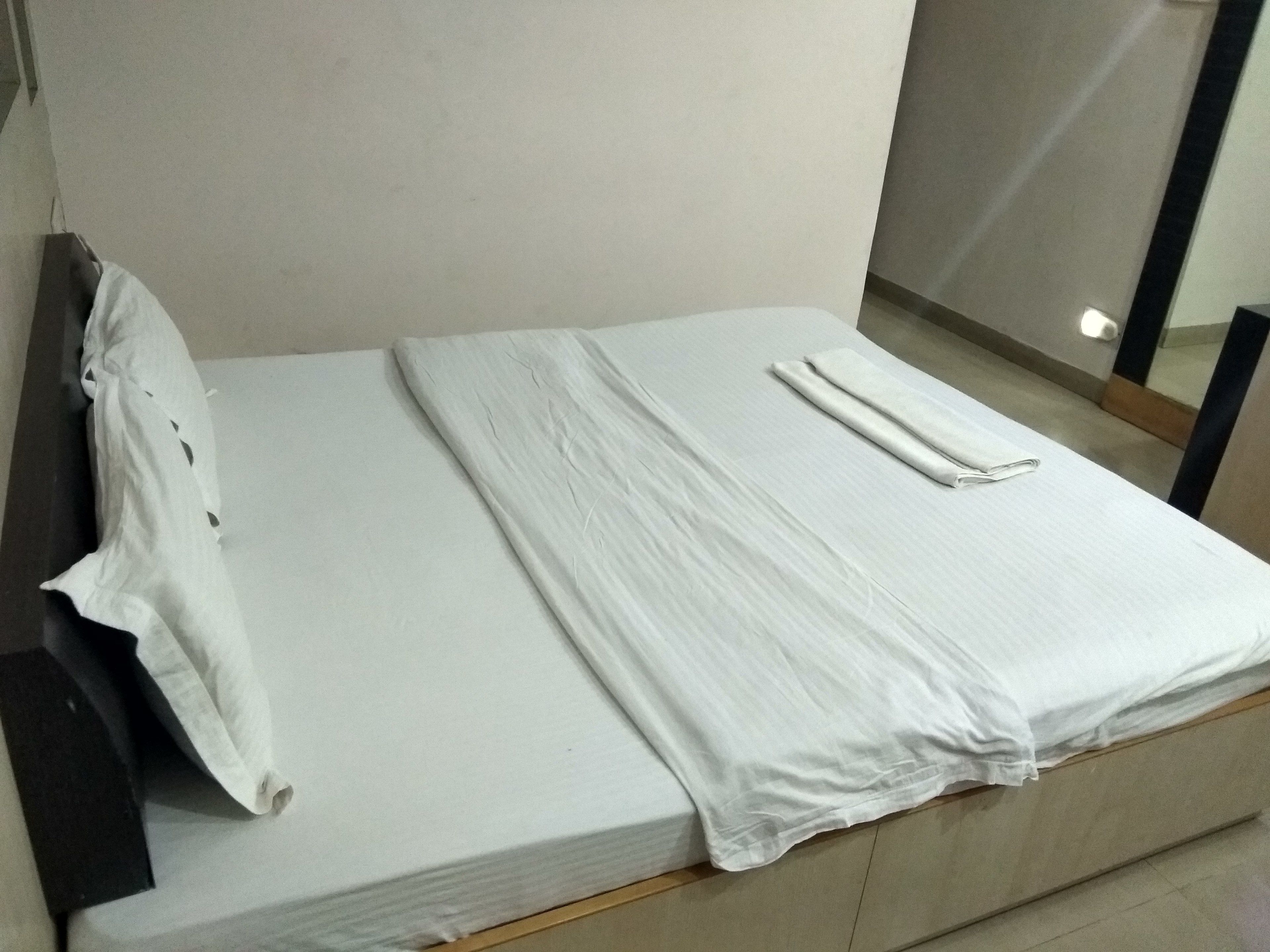 A neatly made bed with a white sheet and pillow, a folded blanket, and a wooden headboard.