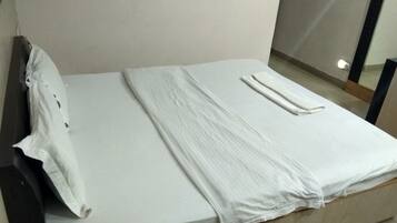 A neatly made bed with a white sheet and pillow, a folded blanket, and a wooden headboard.