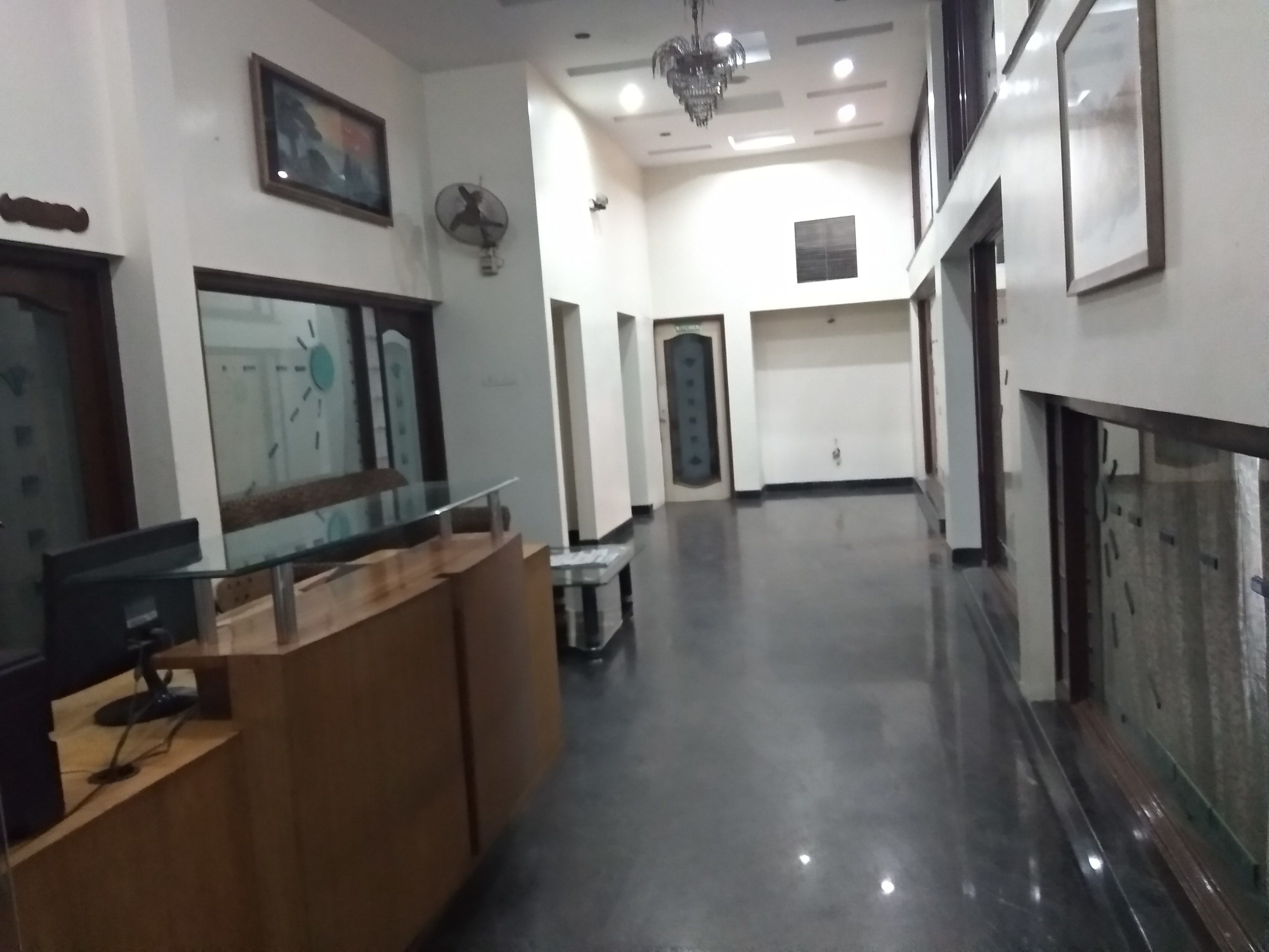 Zona de recepción con separador de vidrio, mostrador de madera y ventilador de techo.