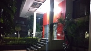 A building with a staircase leading to a red and white entrance, surrounded by greenery.