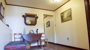 A hallway with a wooden floor, a wooden bench, a small table with a clock, and a mirror on the wall.