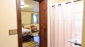 A bedroom with a bed, a chair, a mirror, and a shower curtain.