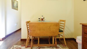 A dining area with a wooden table and chairs, a rug, and a painting on the wall.