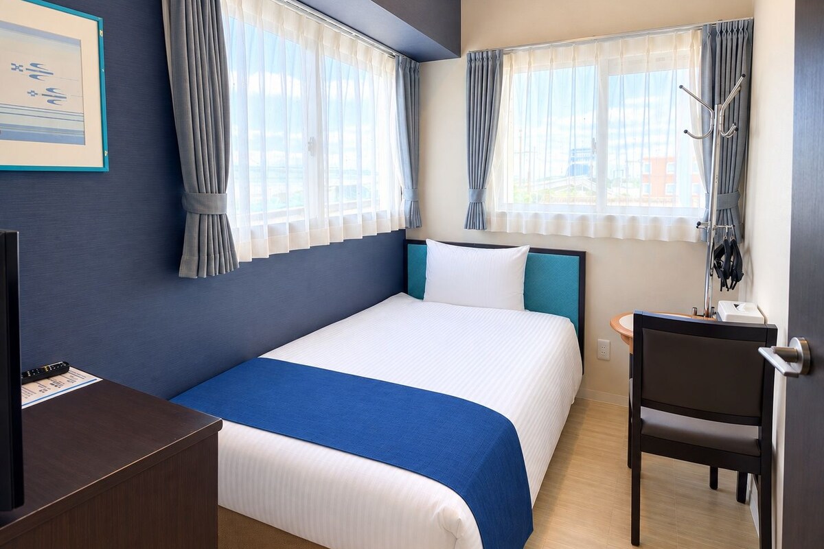 Une chambre d’hôtel avec un lit, un bureau, une chaise et une fenêtre avec des rideaux.