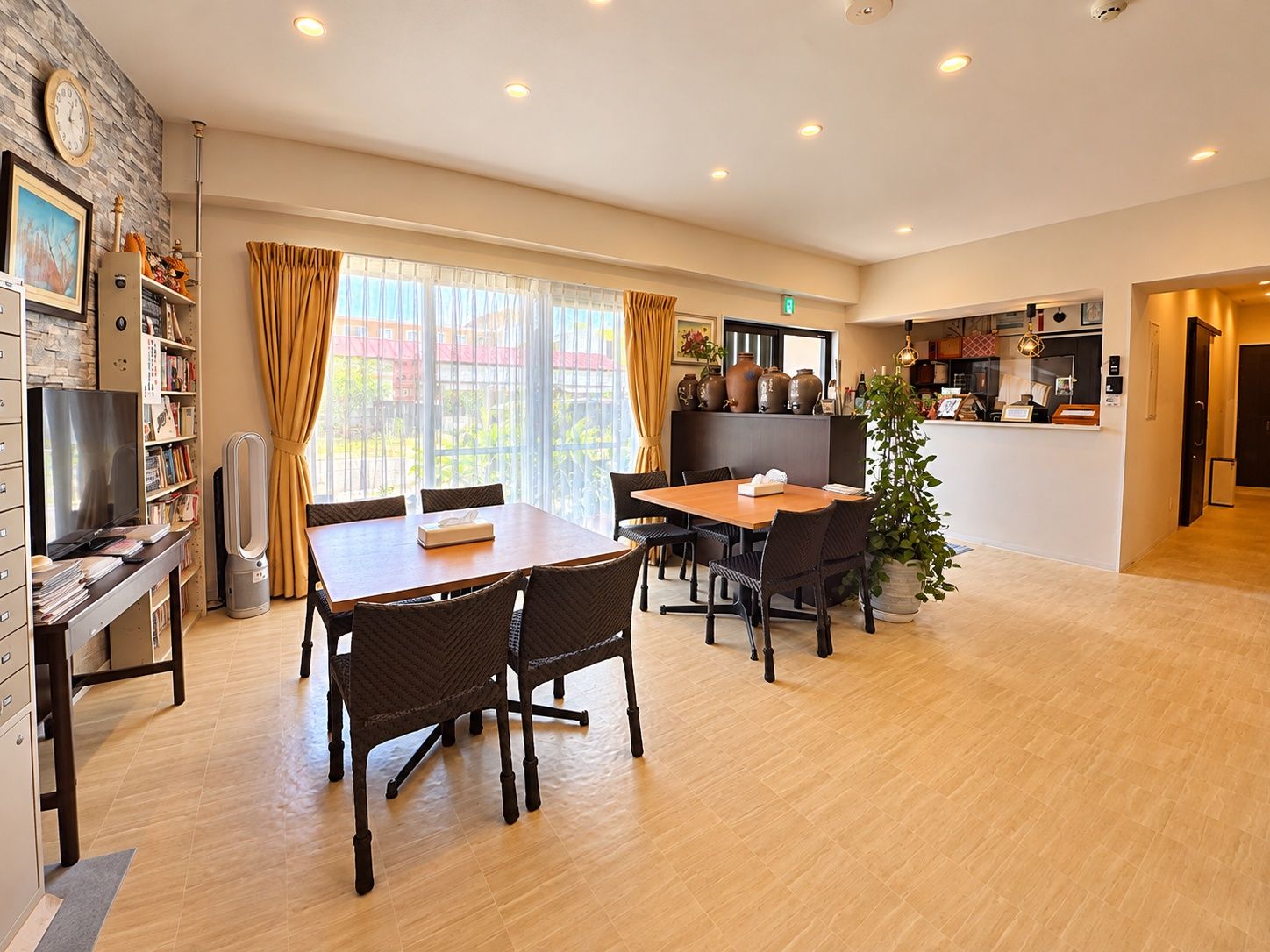 A hotel room with a dining area, a TV, a bookshelf, and a large window with curtains.
