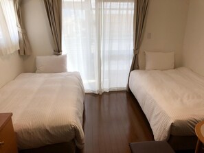 A room with two single beds, a wooden floor, and a small wooden table.