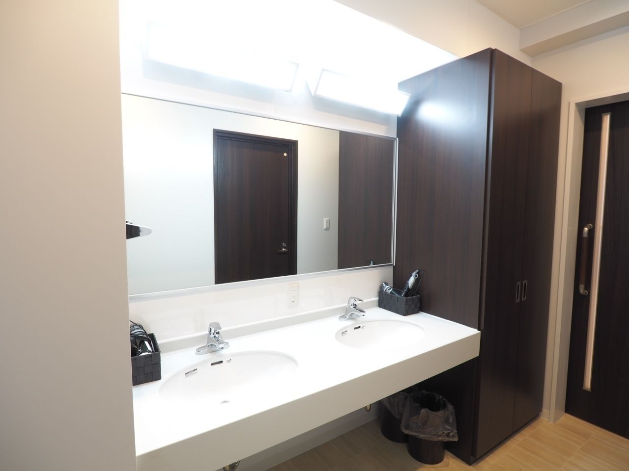 A modern bathroom with two sinks, a large mirror, and dark wooden cabinets.