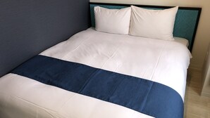 Ein ordentlich bezogenes Bett mit weißer und blauer Bettwäsche, ein türkisblaues Kopfstück und eine schlichte Wand.