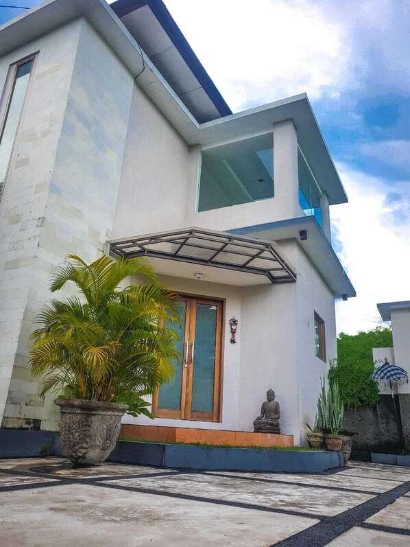 A modern two-story house with a large glass door, a small statue in front, and a potted plant to the left.