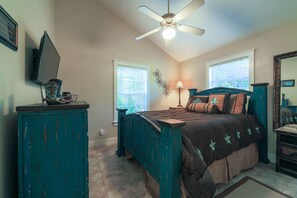 A bedroom with a bed, a ceiling fan, a dresser, a TV, and two windows. - Abby's Place 5 - Cowgirl Up! (Fredericksburg)