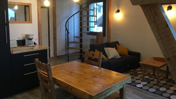 A cozy kitchen with a wooden table and chairs, a built-in oven, and a coffee maker. There is a spiral staircase leading to an upper level.