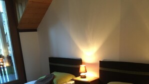 Two single beds with white linens, a nightstand with a lamp, and a window with a view of the outside.