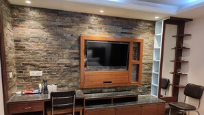 Un espacio habitable compacto con pared de piedra, televisor integrado, pequeña cocina americana y zona de estar.