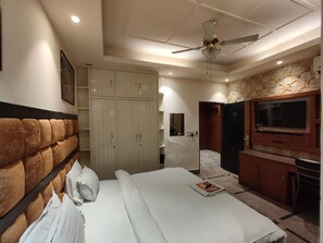 Quarto de hotel com cama, guarda-roupa, televisão e ventoinha no teto.