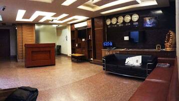 A lobby with a reception desk, a black sofa, a wooden bench, and a clock on the wall.