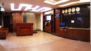 Un vestíbulo con mostrador de recepción, un televisor y una pared con relojes.
