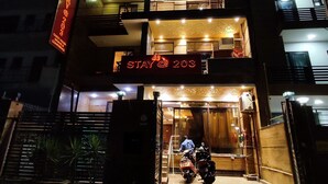 Entrada de un hotel con un letrero de neón que dice "STAY @ 203" y un cartel que indica "GUEST HOUSE".