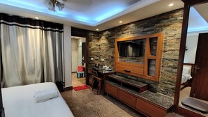 Habitación de hotel con cama, televisión montada en una pared de piedra, escritorio con silla y baño visible a través de una puerta abierta.