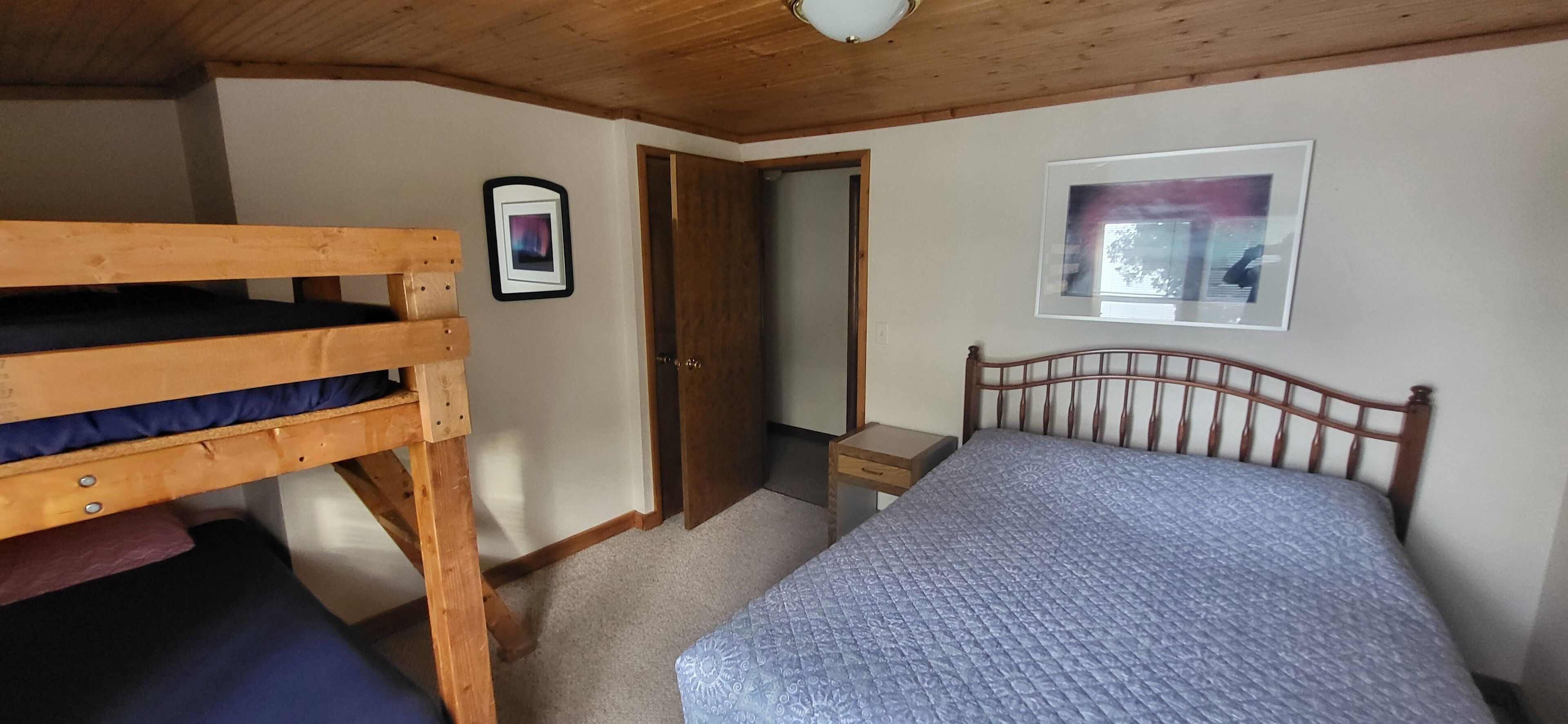Una habitación con una cama individual, una litera, una mesita de noche pequeña y una puerta que da a otra habitación.