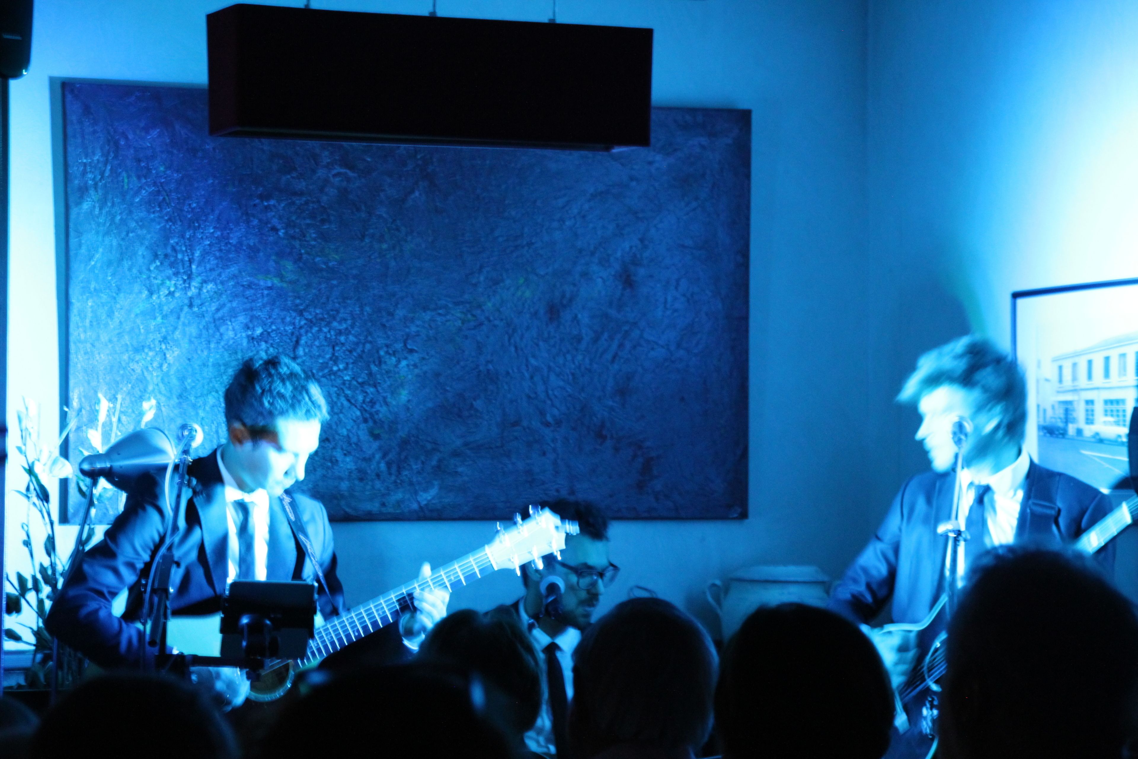 Een band treedt op het podium, met een groot abstract schilderij op de achtergrond.
