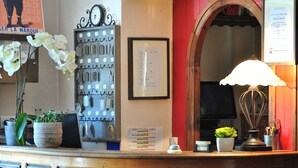 Un mostrador de recepción con un reloj, ganchos para llaves, un menú enmarcado y elementos decorativos.