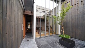 Ein modernes Gebäude mit Holzfassade, Glastür und einem kleinen Gartenbereich mit Pflanztopf und Baum.