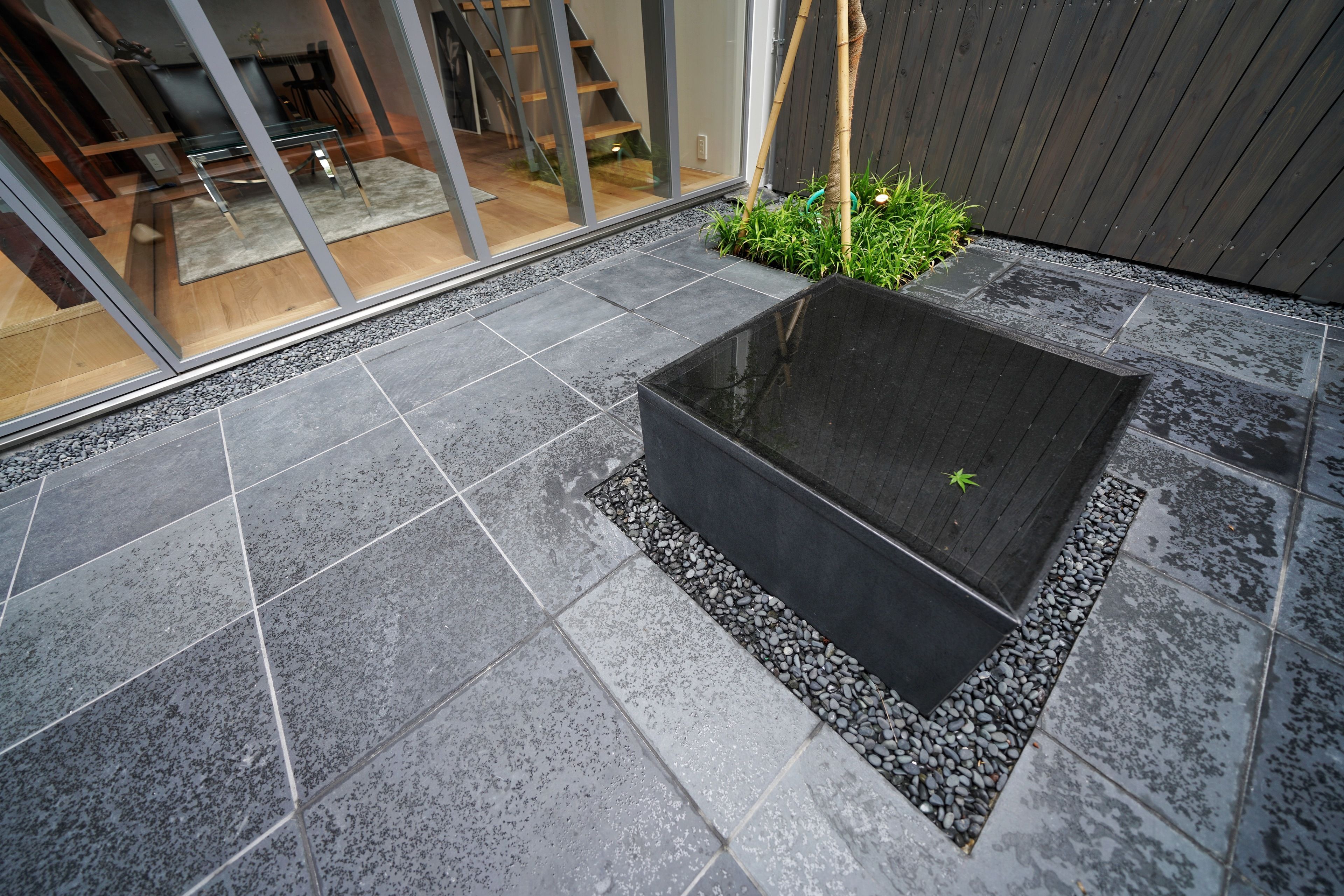 Un espace extérieur moderne doté d’un bassin rectangulaire, entouré de carreaux gris et de galets.