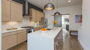 Une cuisine moderne avec des meubles en bois, un îlot central agrémenté d’un saladier de fruits et des luminaires suspendus.