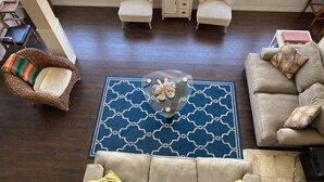 A spacious living room with a large window, a blue patterned rug, a beige sofa, a wicker chair, and a small wooden table. - Catalina's Premier Bay View Vacation Home (Avalon)