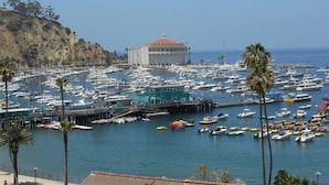 A marina with numerous boats docked, a prominent building with a dome, and palm trees lining the water. - Catalina's Premier Bay View Vacation Home (Avalon)