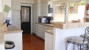 A compact kitchen with white cabinets, a microwave, and a coffee maker on the counter. There is a trash bin and a small stool near the window. - Catalina's Premier Bay View Vacation Home (Avalon)