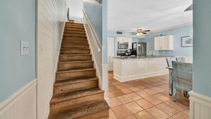 A kitchen with a central island, white cabinetry, and a dining area with wicker chairs. - Discover Blue Surf 9, Pet-Friendly 2BR Townhouse Beach Service Included Miramar Beach! (Destin)