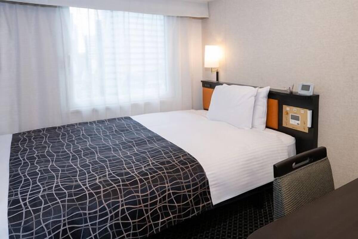 Une chambre d’hôtel avec un lit, une table de chevet, une lampe et une fenêtre avec des rideaux.