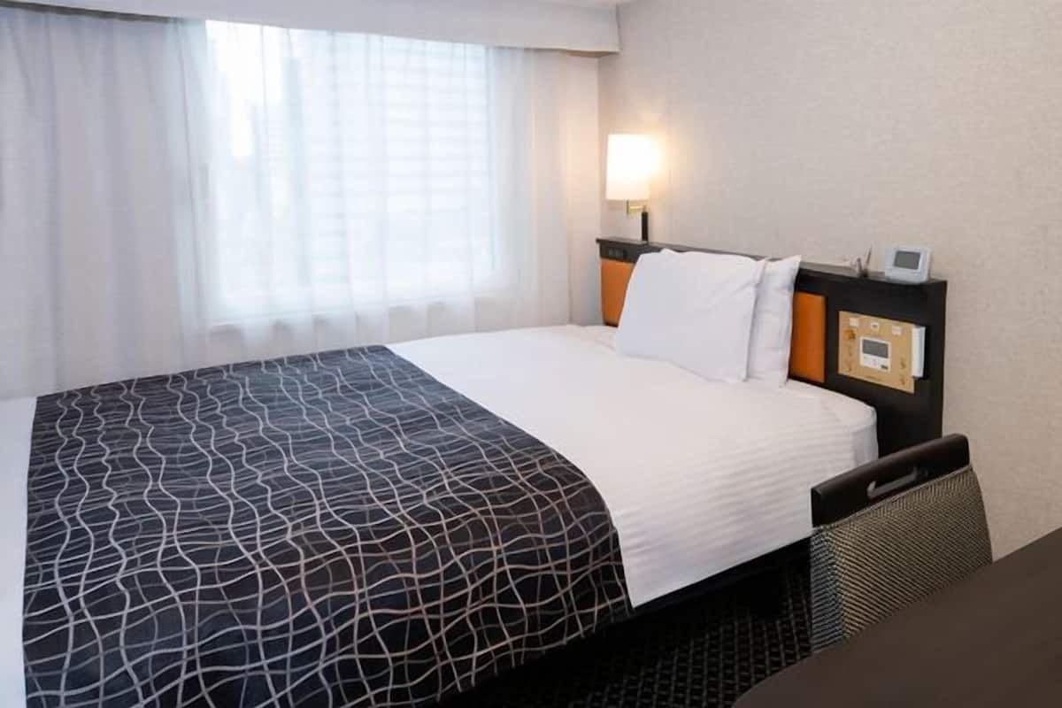 Ein Hotelzimmer mit Bett, Nachttisch, Lampe und einem fenster mit Vorhängen.