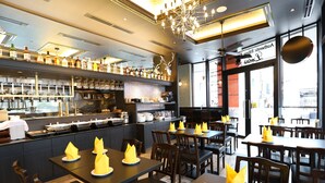 A restaurant interior with tables set with yellow napkins, a bar area with bottles and glasses, and a chandelier. - APA Hotel Shinjuku Kabukicho Chuo (Tokyo)