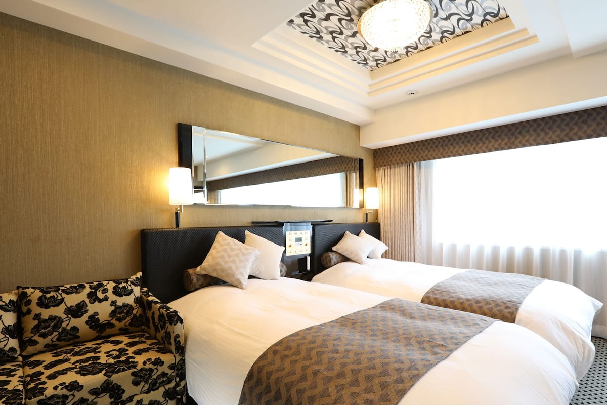 Une chambre d’hôtel avec deux lits, un canapé, un grand miroir et un lustre.