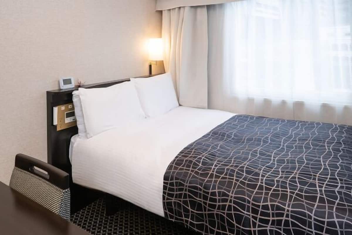 Une chambre d’hôtel avec un lit, un bureau, une table de chevet avec une horloge et une fenêtre avec des rideaux.