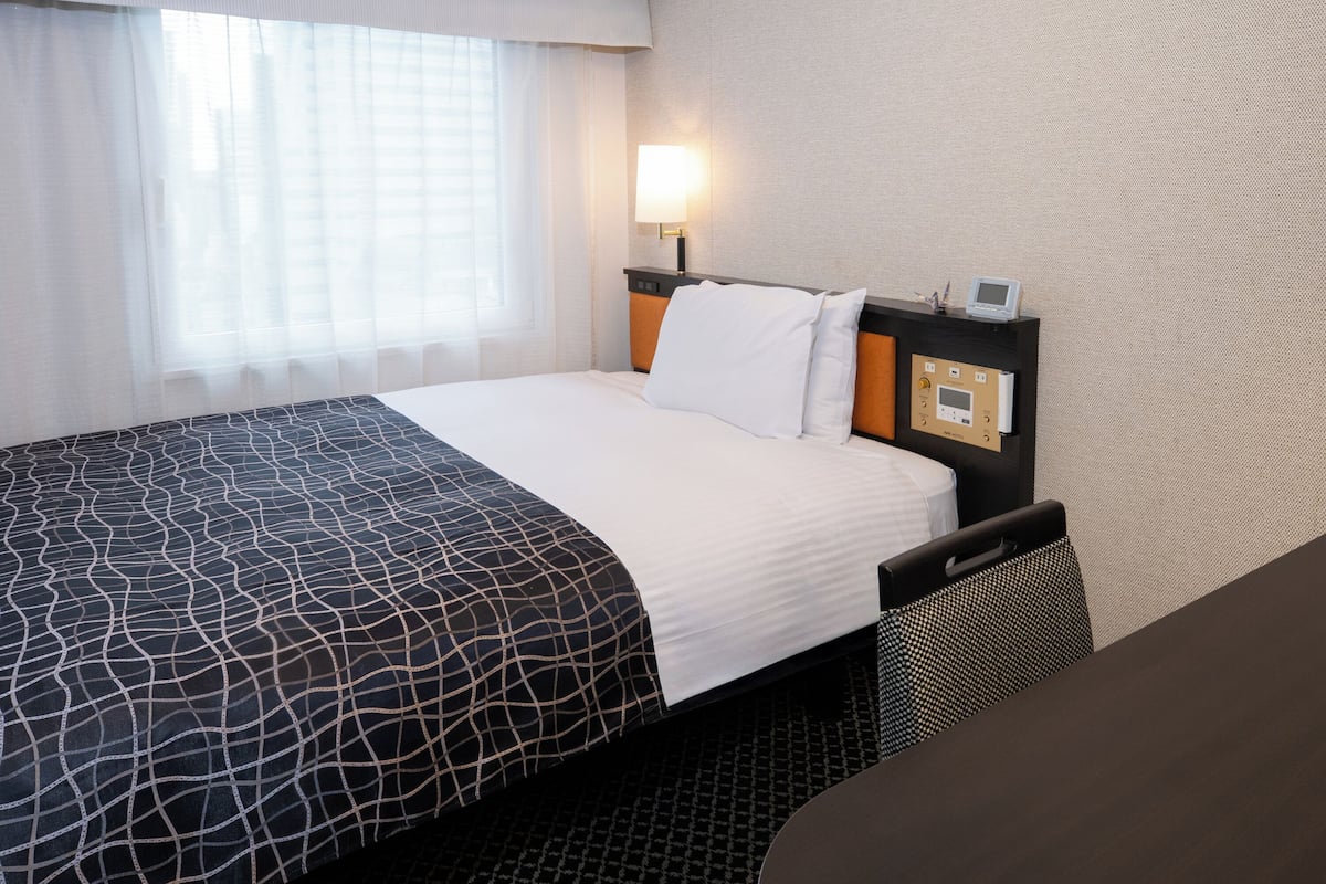 Une chambre d’hôtel équipée d’un lit, d’une table de chevet, d’une lampe et d’un panneau de commande sur la tête de lit.