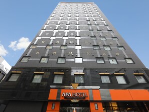 Um edifício alto de hotel com design moderno, destacando uma placa laranja grande para APA HOTEL.