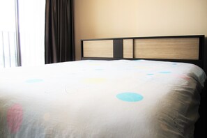 A bed with a patterned bedspread, a headboard with a wooden panel, and a window with curtains.