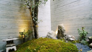 Un jardin intérieur paisible, avec un sol recouvert de mousse, une lanterne en pierre et un arbre.