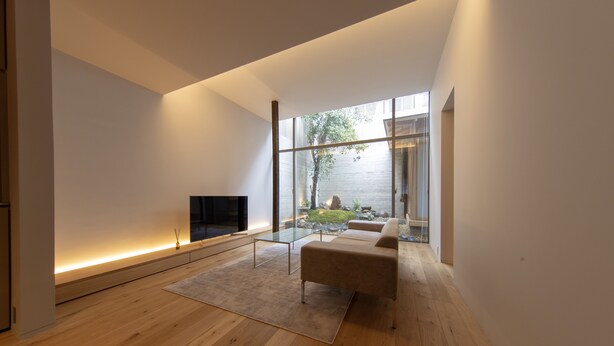 Un salon moderne avec un plancher en bois, un canapé beige, une table basse en verre et un téléviseur à écran plat.